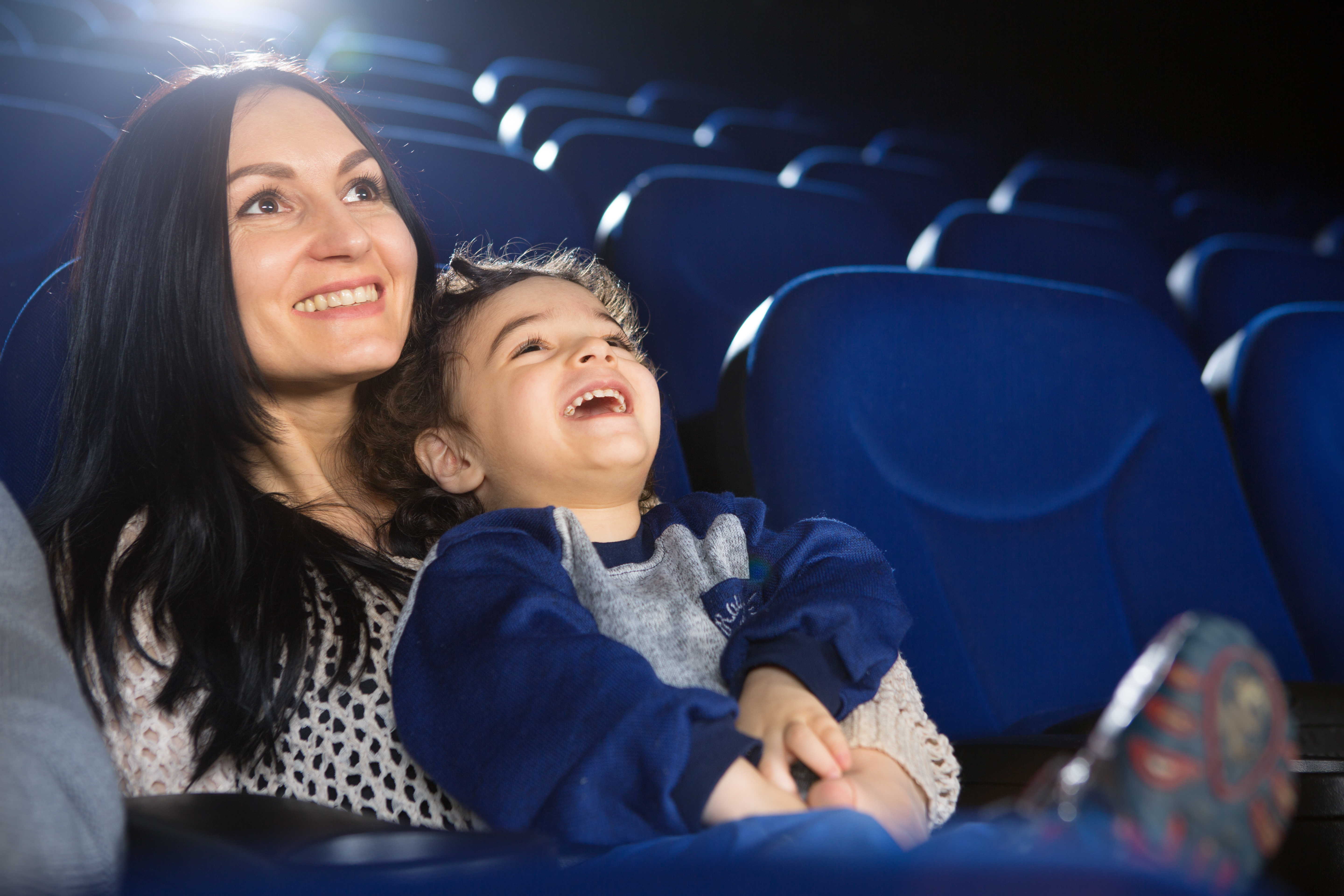 A mum and child sitting in a cinema looking at the screen and smiling