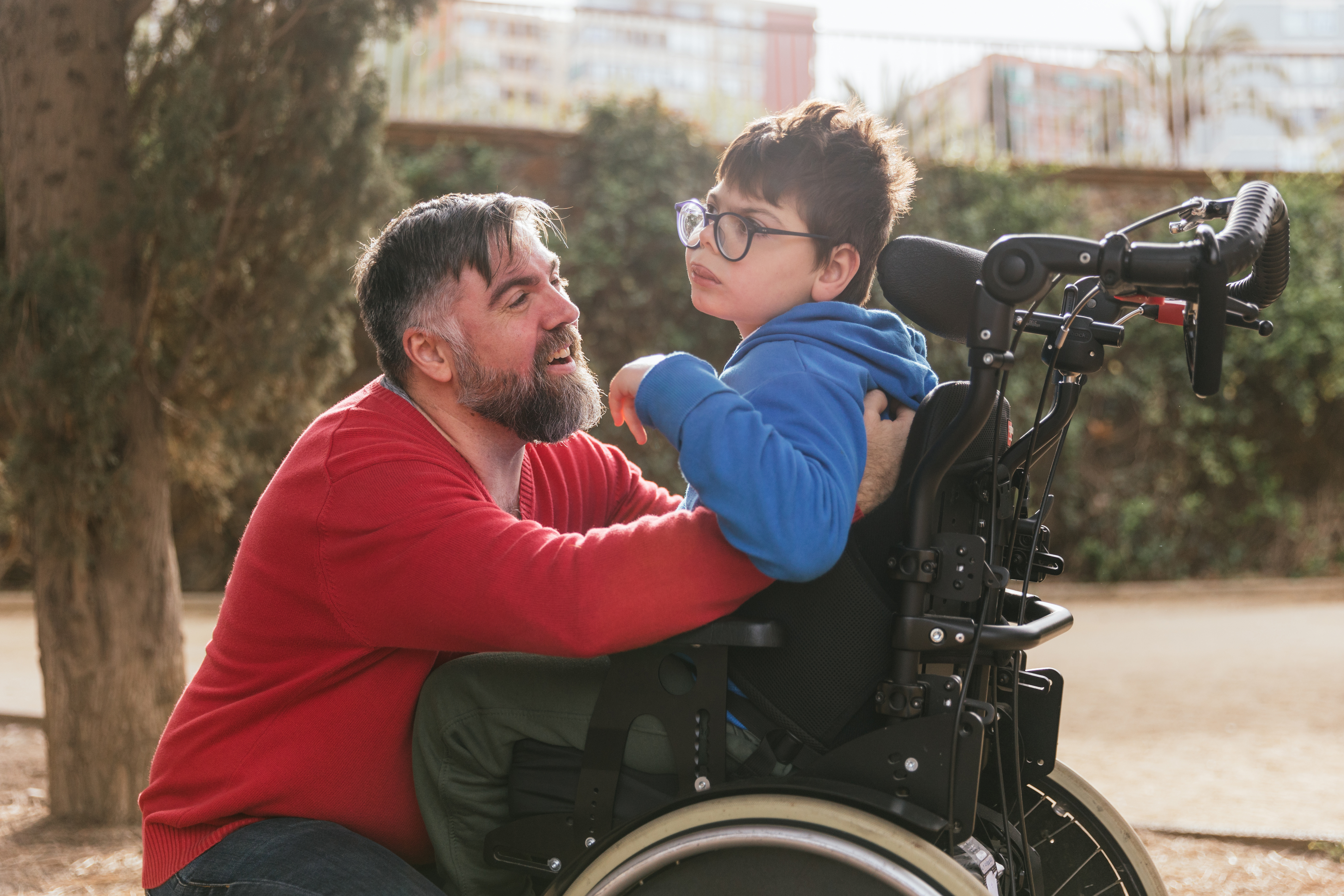 A dad with his arms around his child, who is sitting in a wheelchair