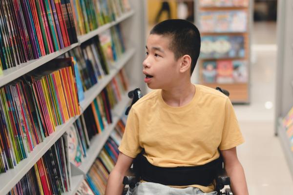 A boy looking at books in a library, and using a wheelchair 