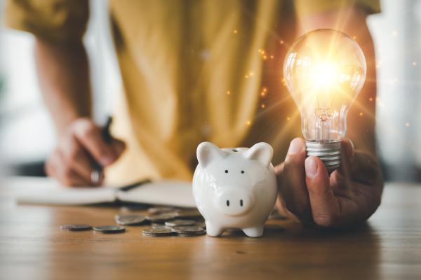 A piggy bank with cash, and a person holding a lit light bulb