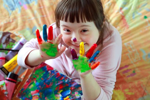 A smiling girl with colourful paint on her hands making a finger painting