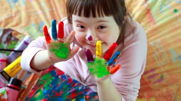 A smiling girl with colourful paint on her hands making a finger painting